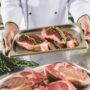 cropped image of african american chef holding tray with raw steaks at restaurant kitchen