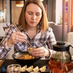 Girl eating Japanese food with chopsticks in restaurant